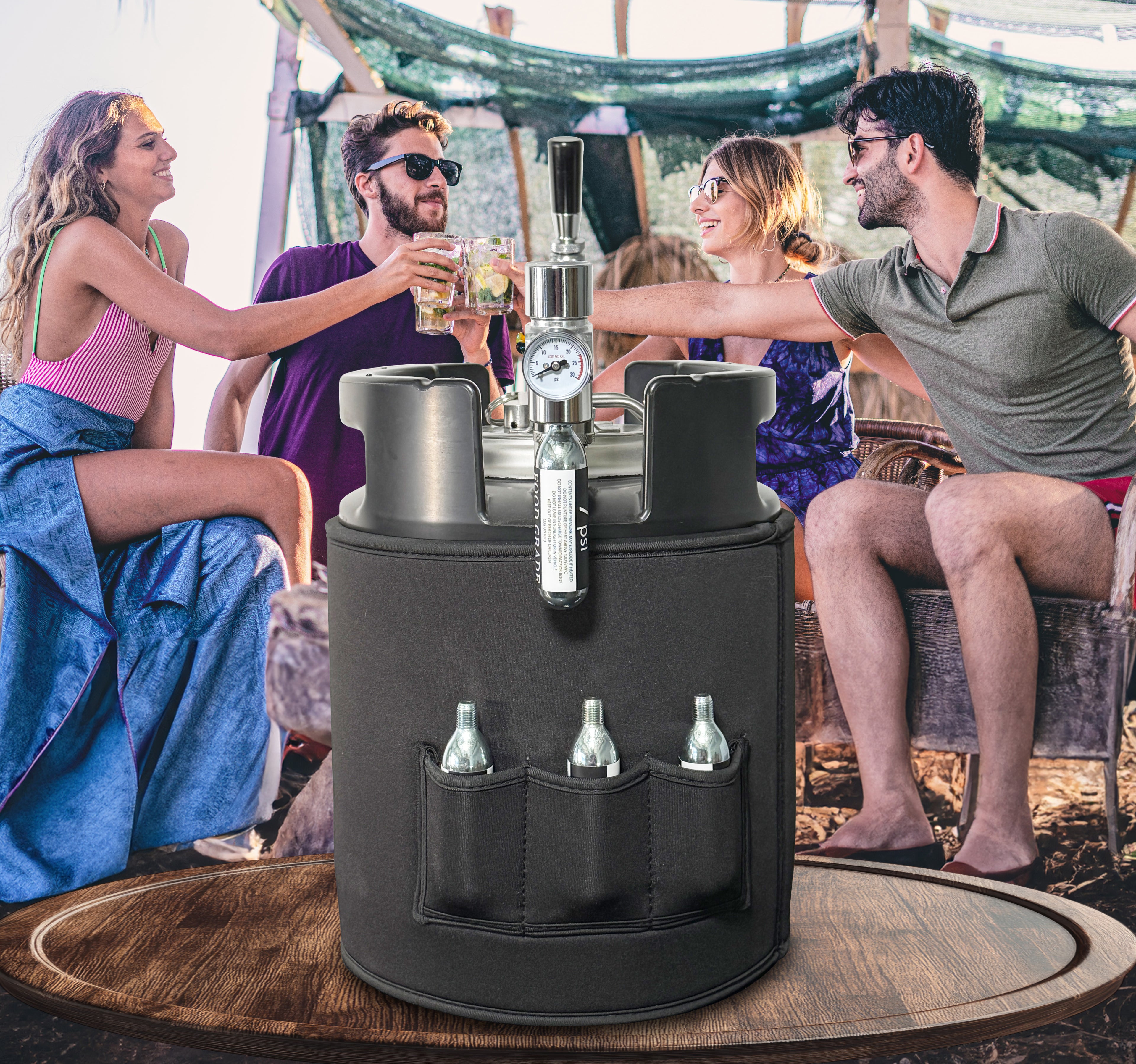 Backside of black portable 7L Gloria Keg showing co2 regulator and extra cartridges in pockets of neoprene sleeve on a table, surrounded by people enjoying drinks outdoors